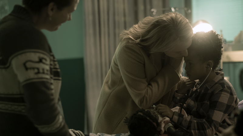 A judgmental nurse looks on as Offred comforts her daughter.